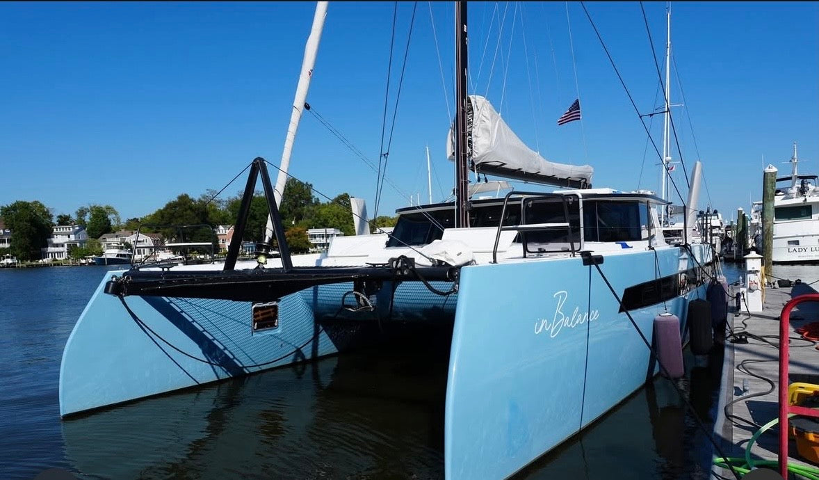 Light blue catamaran with glossy hulls docked at a marina under a clear blue sky